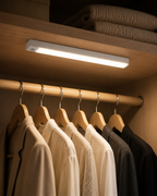 Barre LED LUMEQIA installée dans une penderie, éclairant des vêtements suspendus sur cintres